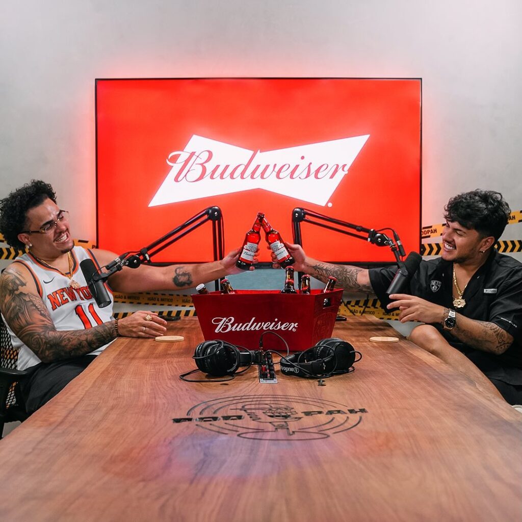 Igão (esq.) e Mítico, do podcast Podpah, em estúdio celebram ação com Budweiser; dulpa estará no Lollapalooza